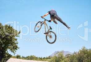 Man showing his cycling skills while out cycling on a bicycle outside. Adrenaline junkie practicing a dirt jump outdoors. Male wearing a helmet doing tricks. Unrecognizable passionate guy having fun