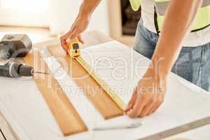 I dont need this entire piece. Cropped shot of an unrecognisable construction worker standing alone and using measuring tape to measure a beam of wood.