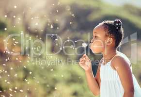 Happy little african american girl blowing dandelion flower outside. One cheerful black child having fun playing at the park during spring on a sunny day. Allergy free concept