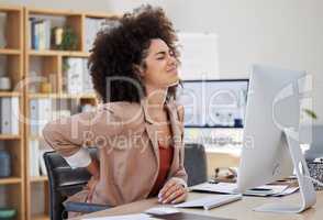 One young mixed race business woman with an afro suffering from back ache while sitting at her desk in the office at work. A beautiful african american entrepreneur struggling with cramp and pain