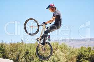 Man showing cycling skills while out cycling on a bicycle outside. Adrenaline junkie practicing a dirt jump outdoors. Male wearing a helmet doing tricks with a bike. Having fun doing extreme sports