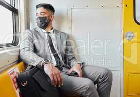 Who wouldve thought that life would be like this. a young businessman wearing a face mask while staring out the window on a train during his commute.