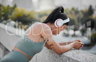 Young mixed race sportswoman wearing headphones listening to music and taking a break from running outside in the city. Exercise is good for your health and wellbeing