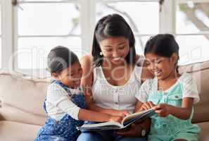 Females only reading a book together on the sofa at home and looking relaxed and happy while enjoying family time with their young mother