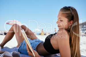 One beautiful young caucasian woman relaxing on the beach. Enjoying a summer vacation or holiday outdoors during summer. Taking time off and getting away from it all. Reading alone on the sand outside