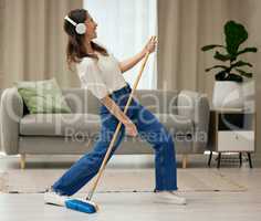 Nothing quite like being in your own space. a young woman singing while sweeping the floors at home.