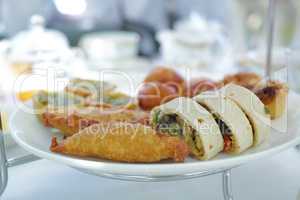 A plate of snack food or starters on a hotel buffet table or formal event on a sunny day inside. Different savory pastries, pies and fried dumplings on a ceramic serving dish at a modern dinner party