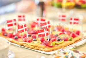 Danish fruit pastry for dessert to celebrate patriotism on Constitution Day in June. Annual holiday feast in Denmark with national flags in food. Fresh summer produce on a baked puff pastry