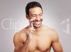 Handsome young mixed race man posing shirtless in studio isolated against a grey background. Hispanic male using a dermal face roller to massage and relax his skin. All part of his skincare regime