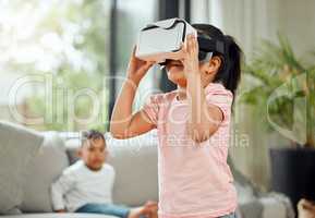 A countdown to the end of a quiet storm. a little girl playing with a virtual reality headset while her brother watches from the sofa at home.