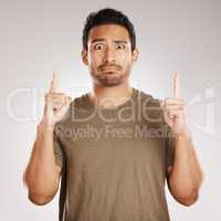 Handsome young mixed race man pointing towards copyspace while standing in studio isolated against a grey background. Unsure hispanic male advertising or endorsing your product, company or idea