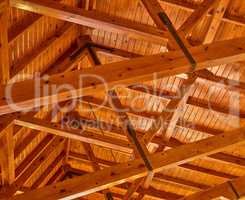 Crossed wood support trestles with their angle supporters on a ceiling. Closeup of roof rafters and cross beams of a shelter. Crossed thick beige crossbeams boards for building and construction