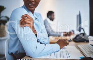 Closeup of one stressed african american businesswoman suffering with arm and shoulder pain in an office. Entrepreneur rubbing muscles and body while feeling tense strain, discomfort and hurt from bad sitting posture and long working hours at desk