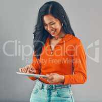 Smiling mixed race woman using digital tablet while isolated against grey studio background with copyspace. Happy young hispanic standing alone while browsing the internet and networking on technology