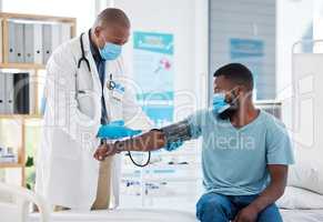 Doctor checking the blood pressure of a patient using a cuff and monitor. African american doctor reading a patients blood pressure. Medical gp and patient wearing masks to protect from covid