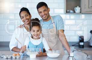 Portrait of a loving hispanic family baking together at home. Adorable little girl mixing ingredient in the kitchen with the help of her parents