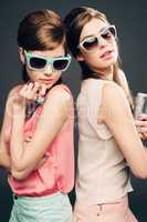 My sister from another era. Studio shot of two attractive young women dressed up in 60s wear against a dark background.