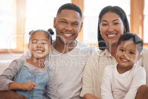 Portrait of a smiling young family of four at home. Mixed race mother and father bonding with their son and daughter on a weekend inside. Hispanic boy and girl enjoying free time with their parents