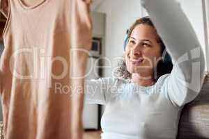 Woman listening to music in headphones. Young woman looking at fresh, cleaned laundry. Happy woman holding washed top. Young woman enjoying music and housework chores. Woman cleaning her clothing