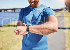 Fit hispanic athlete checking his smartwatch to track his progress while running outside. Athletic man checking the time on his watch while jogging by a river. Smiling man exercising outside.