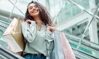 Portrait beautiful mixed race woman standing on an escalator while shopping in a mall. Young hispanic woman carrying bags, spending money, looking for sales and getting in some good retail therapy