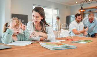 Adorable little caucasian girl sitting at table and doing homework while her mother helps her. Beautiful serious young woman pointing and teaching her daughter at home. Parent home schooling her child