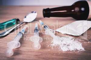 A spoon and syringes filled with narcotics and an open beer bottle on a wooden table. Heroin is a highly addictive drug made from morphine used as a narcotic. Alcohol abuse can lead to addiction