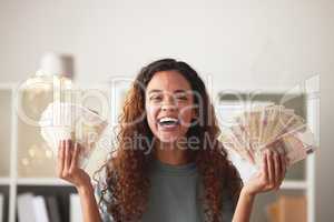 Beautiful young african american woman holding stacks of paper money while standing in her living room at home. Happy mixed race female showing off the return on investment and savings while smiling