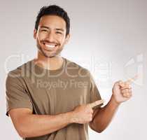 Handsome young mixed race man pointing towards copyspace while standing in studio isolated against a grey background. Happy hispanic male advertising or endorsing your product, company or idea