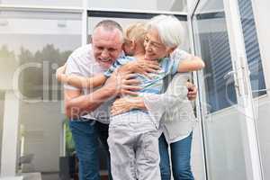 Senior grandparents hugging their small grandson at home. Little boy bonding and embracing smiling grandmother and grandfather. Adopted child feeling happy and grateful while hugging elderly couple