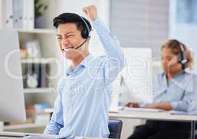 One happy young asian male call centre telemarketing agent cheering with joy and punching the air with fists while working in an office. Excited businessman celebrating successful sales and reaching targets to win