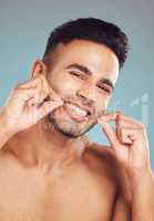 Portrait of one smiling young indian man flossing his teeth against a blue studio background. Handsome guy grooming and cleaning his mouth for better oral and dental hygiene. Floss daily to prevent tooth decay and gum disease