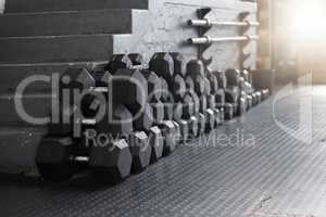 Closeup of a group of gym weights on the floor in an empty health and sports club. Macro view of dumbbells barbell weights in a dark exercise room. Get to the gym to increase your health and fitness