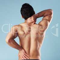 Rearview young mixed race man standing shirtless in studio isolated against a blue background. Unrecognizable topless male athlete suffering from back pain or ache. Hes picked up a fitness injury