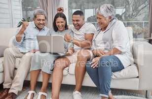 Happy and affectionate mixed race family of four using a laptop to watch sports and cheer on their favourite team in the home living room. Married couple sitting with their mature parents on the sofa