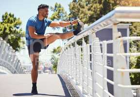 Fit athletic mixed race man stretching on a bridge in the city during his workout. Young hispanic man doing warm up exercises outdoors on a sunny day. Warming up before starting is endurace and cardio