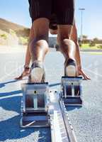 Feet of athlete in starting position on a running track. A male track and field runner ready to leave the starting block to start his sprint. Sportsman with hands on the starting line during a race
