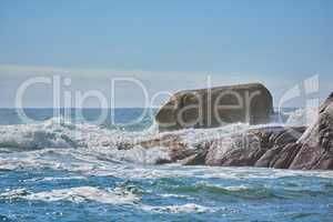 Copy space of a turbulent sea with rough tides and choppy waves from strong winds crashing onto big boulders at the beach with a clear blue sky background. Rocky coast in Camps Bay, South Africa