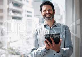 I manage my teams schedule. a mature businessman standing alone in the office and using a digital tablet.