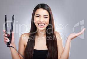 It really is a wonder tool for women. Studio portrait of an attractive young woman using a flat iron to straighten her hair against a grey background.