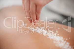 Caring for her delicate skin. Shot of a masseuse pouring exfoliating salt scrub onto a clients back.