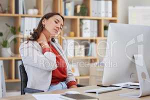 One young mixed race female businesswoman sitting at her desk in front of her computer experiencing neck pain and discomfort in her office. Young asian woman suffering from muscles spasms and tension in her neck while massaging it to release tension