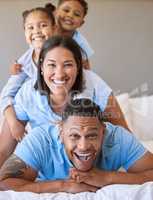 Portrait of a smiling boy and girl lying on their parents in a pile at home. Mixed race couple bonding with their son and daughter. Hispanic siblings enjoying free time with their mother and father