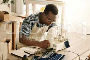 african american tailor sewing a piece of denim. Young designer using his sewing machine. Serious tailor stitching a piece of fabric. Focused seamstress working on his material