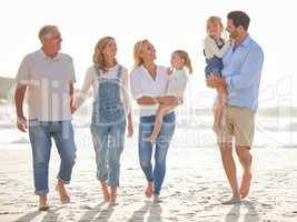 Multi generation family holding hands and walking along the beach together. Caucasian family with two children, two parents and grandparents enjoying summer vacation