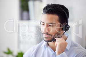 A mixed race man working in a call center. Operator using a wireless headset, consulting online or making a call. A male customer support agent directing calls and operating the switchboard at work