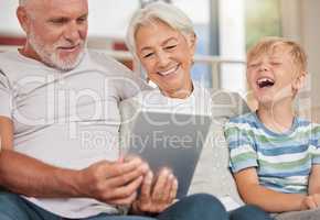 A happy mature couple bonding with their grandchild while babysitting and using a digital tablet for video call at home. Grandparents relaxing with their cute little grandson and browsing