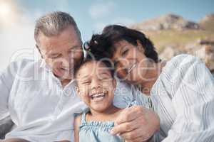 Smiling mixed race grandparents sitting with granddaughter on a beach. Adorable, happy, hispanic girl bonding with grandmother and grandfather outside on weekend. Seniors and child enjoying free time