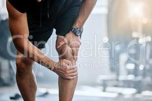 Unknown trainer alone in gym and suffering from knee injury. One coach standing and rubbing leg during workout in exercise health club. One man in fitness centre feeling pain during routine training