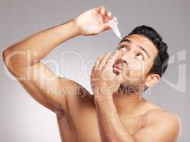 Closeup young mixed race man shirtless in studio isolated against a grey background. Hispanic male applying eyedrops to his eyes. Taking caring of his vision and sight as instructed by the optometrist